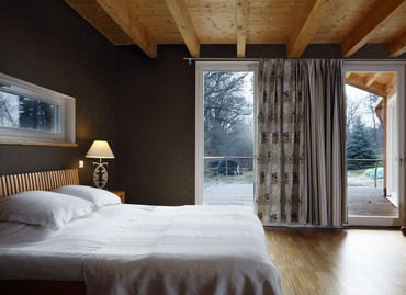 Interiér ložnice rodičů, z manželské postele je výhled přímo do zahrady, obytná terasa je ve stejné výšce jako podlaha v domě
